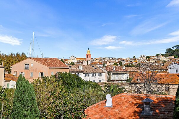 Scenic view of Saint-Tropez featuring terracotta rooftops, lush trees, and the iconic yellow bell tower under a bright blue sky.