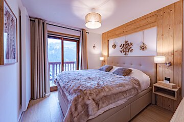 Cozy mountain-themed bedroom featuring a plush bed, faux fur blanket, wooden accents, snowflake decor, and a balcony with a snowy view.