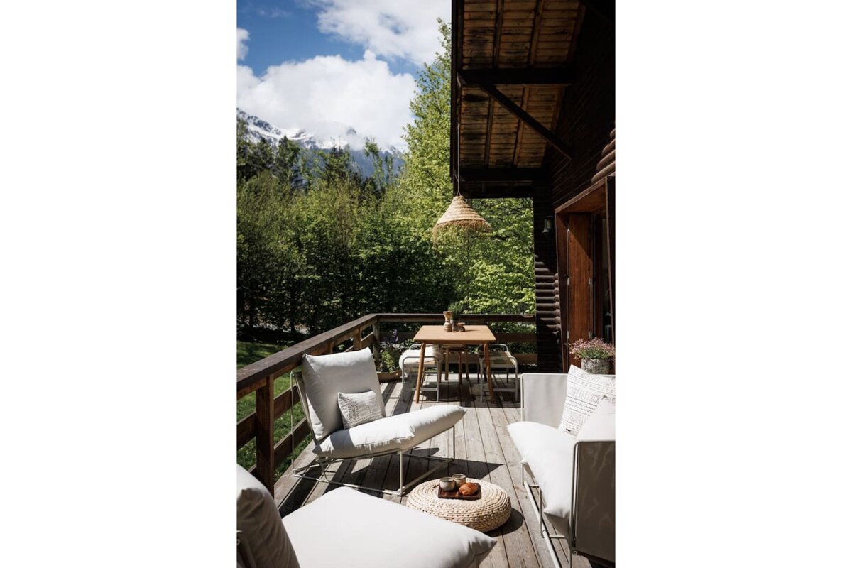 A balcony with chairs and a table with mountains in the background