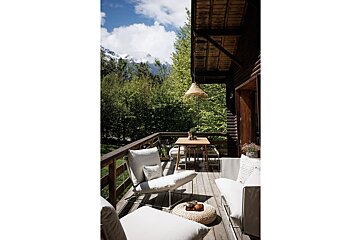 A balcony with chairs and a table with mountains in the background