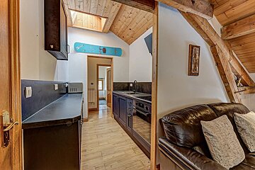 Cozy chalet interior with wood-paneled ceilings, a small kitchen, and a leather sofa in the foreground.