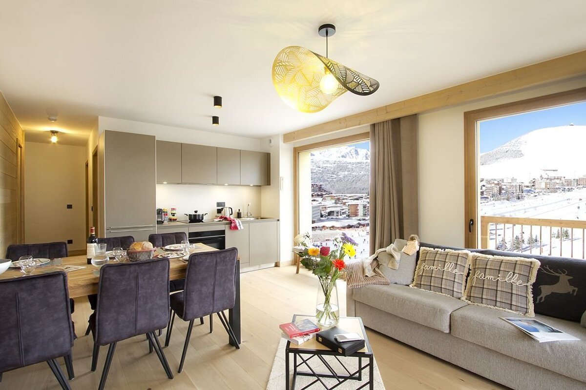 A chic open-plan apartment with dining, kitchen, and living areas. Large windows offer stunning snowy mountain and village views.