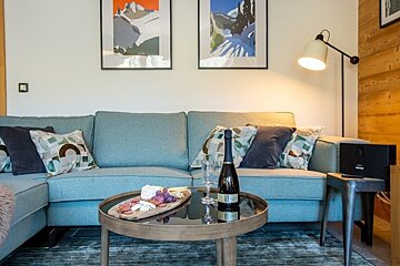 Cozy living room with a teal sofa, framed mountain art, and a coffee table with champagne and a charcuterie board.