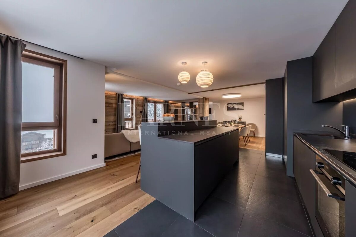 Modern open-concept kitchen featuring a sleek dark grey island, hardwood floors, and stylish spherical pendant lights.