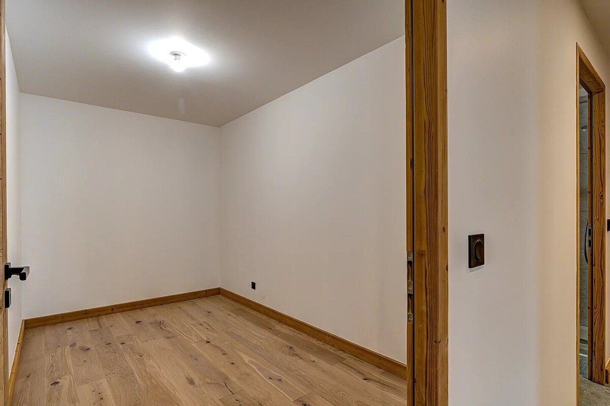 An empty modern room with light wood floors, white walls, and wooden trim, viewed through a doorway.