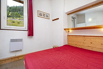 A bedroom with a red bed and a window