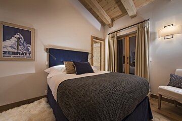 A bedroom with a zermatt poster on the wall above the bed