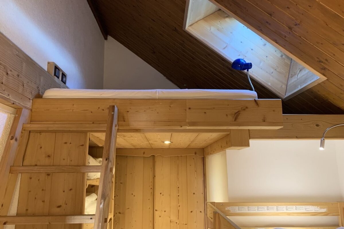 Cozy wooden loft bed with a ladder beneath a slanted ceiling with a skylight.