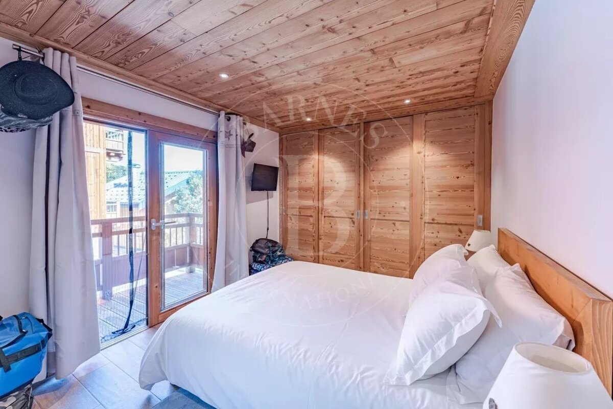 Cozy bedroom with light wood paneled ceiling and closets, a large bed with white linens, and sliding glass doors leading to a balcony.