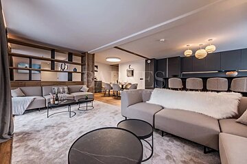 Modern open-plan apartment featuring chic beige sofas, black coffee tables, a dining area, and a sleek kitchen with bar stools.