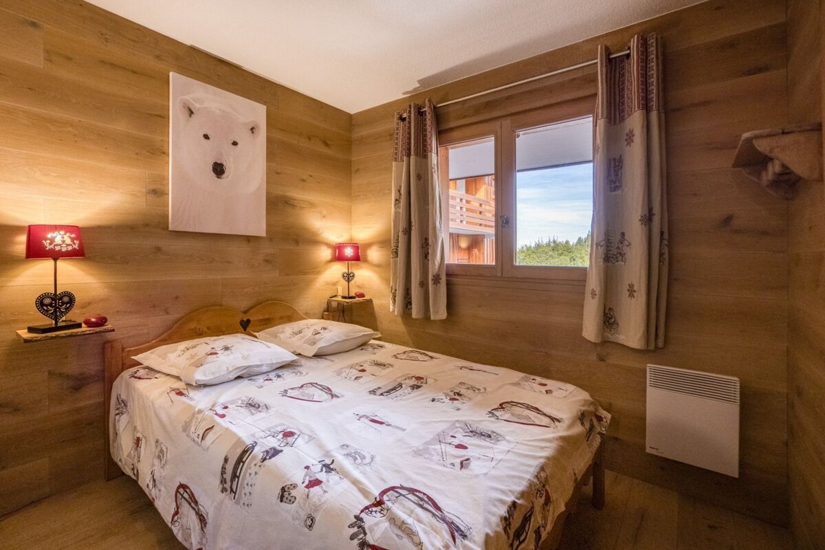 A cozy, wood-paneled bedroom with a double bed, polar bear art, red lamps, and a window overlooking a forest view.