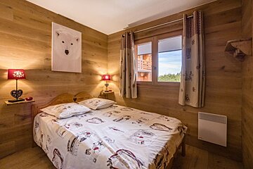 A cozy, wood-paneled bedroom with a double bed, polar bear art, red lamps, and a window overlooking a forest view.
