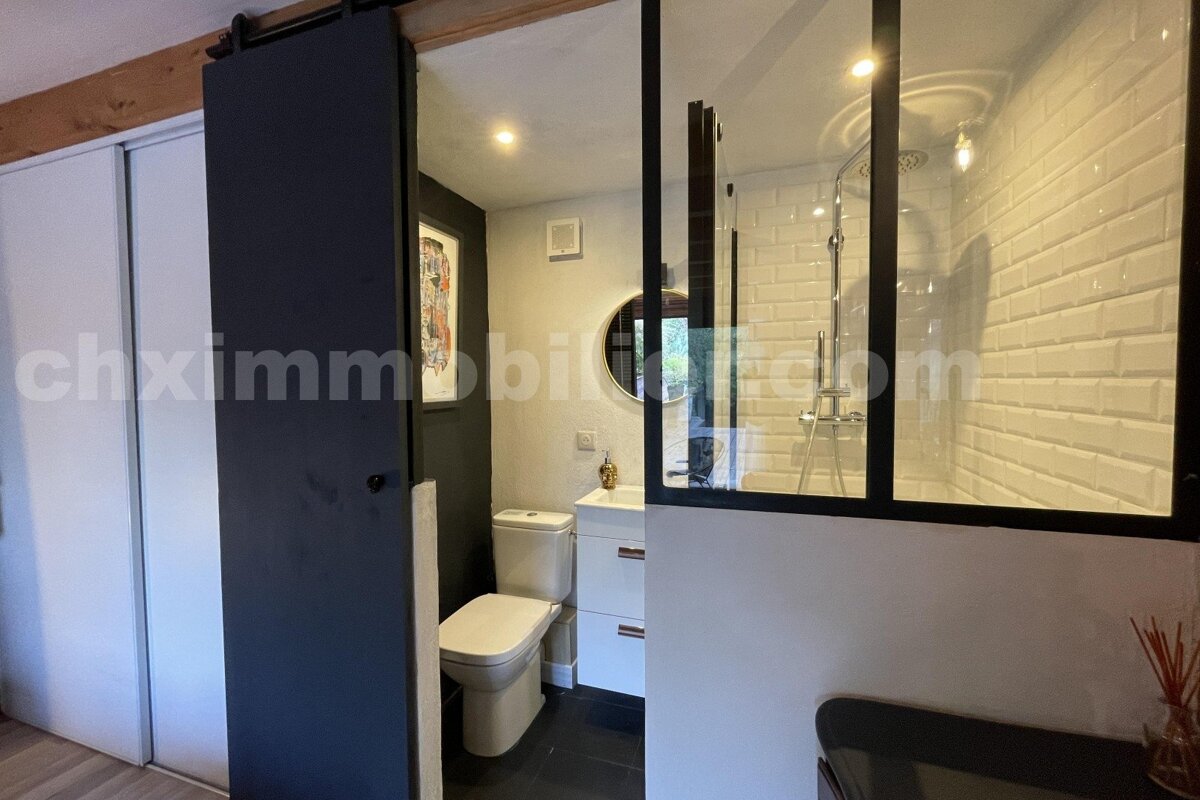 Modern bathroom with dark sliding barn door revealing toilet, sink, and shower with subway tiles and glass partition.
