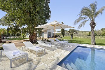 A white umbrella sits on a patio next to a swimming pool