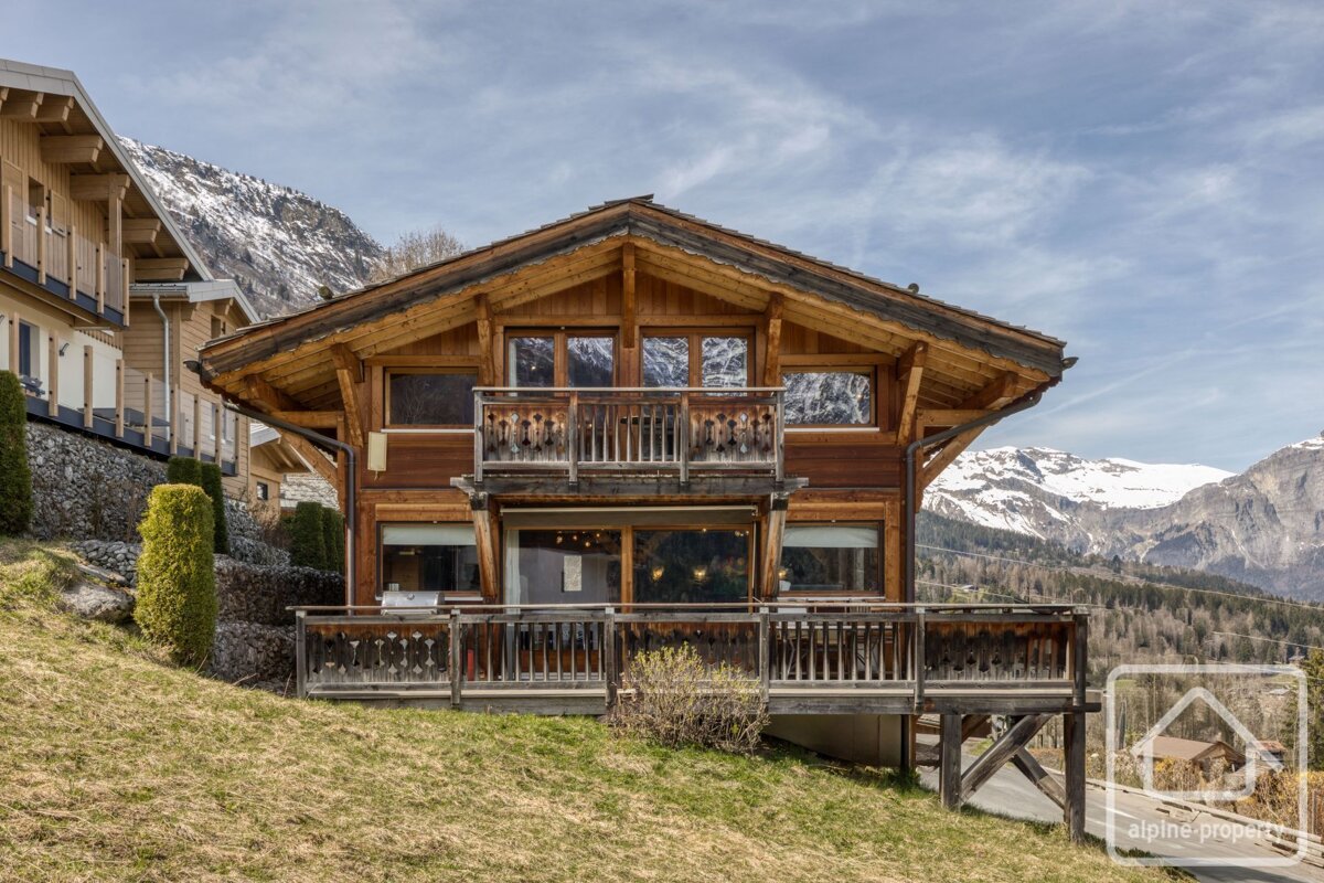 A large wooden house with mountains in the background is for sale by alpine property