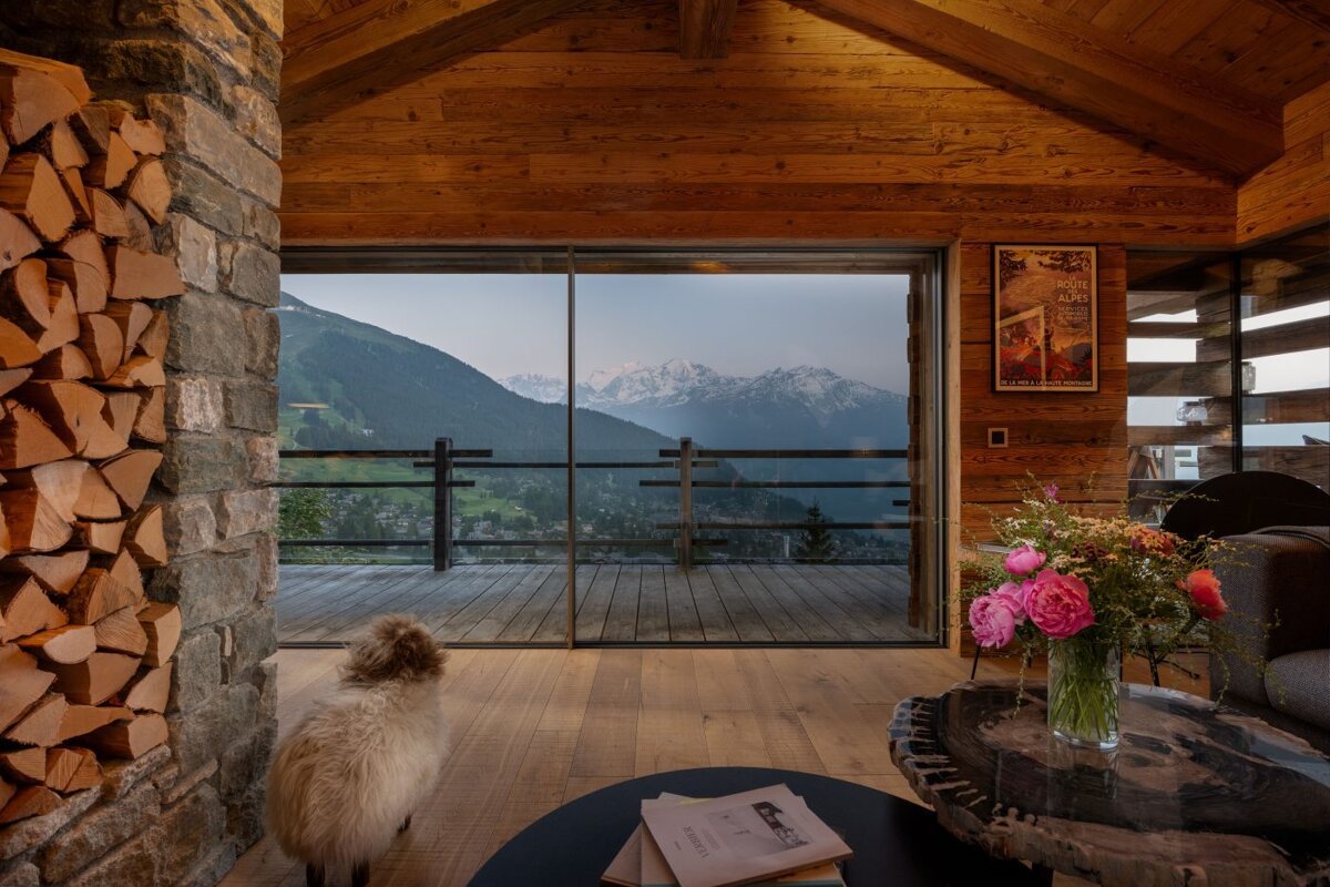 A sheep sits in front of a sliding glass door looking out to the mountains
