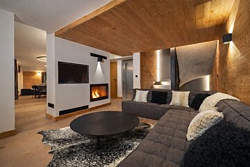 Cozy, modern living room with a large grey sectional, a fireplace, wooden ceiling, and a round black coffee table on a cowhide rug.