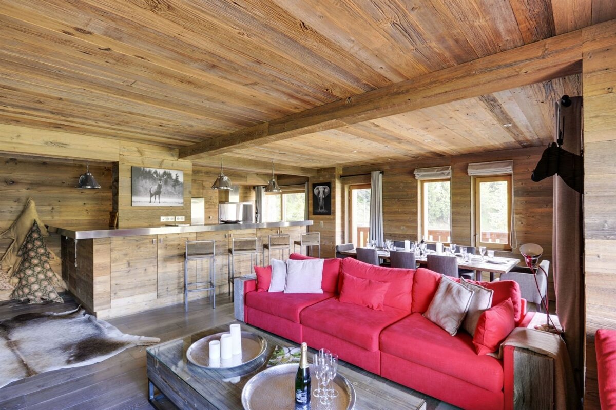 Wood-paneled chalet interior with a bright red sofa, bar, and dining space, creating a cozy yet modern rustic vibe.