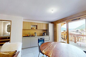 Modern kitchen with wood accents, a round dining table, and a balcony offering mountain views. A bathroom is partly visible.
