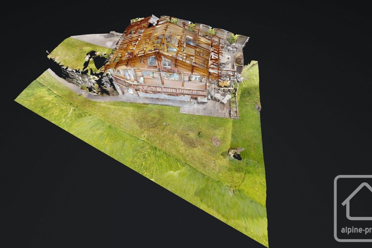 Aerial 3D model of a rustic wooden chalet with exposed roof framing, surrounded by green grass on a dark background.