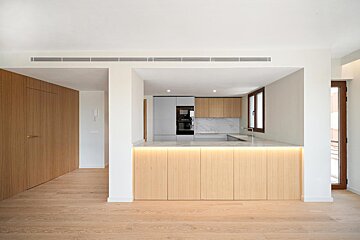 A minimalist open-plan kitchen and living area with light wood accents, white walls, and a sleek island with under-counter lighting.