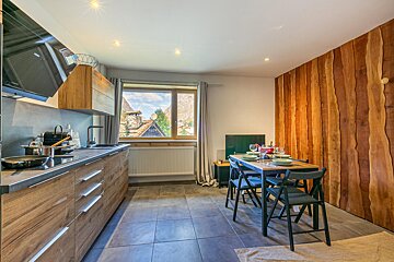 Contemporary kitchen and dining space with wooden cabinets, rustic wood paneling, and a mountain village view from the window.