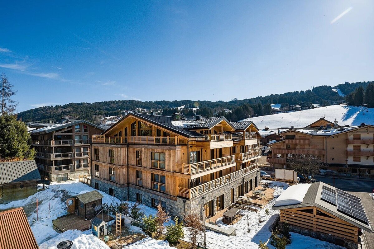 Beautiful wooden chalets in a snowy alpine ski resort under a clear blue sky.