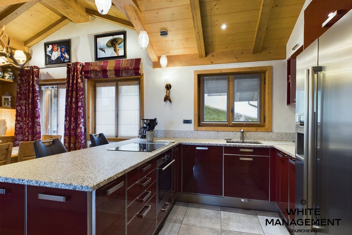 A modern kitchen features deep red cabinets, granite countertops, stainless steel appliances, and a rustic wood-beamed ceiling.