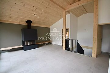 Modern chalet interior with a slanted wooden ceiling, a sleek black fireplace against an olive wall, and a staircase.