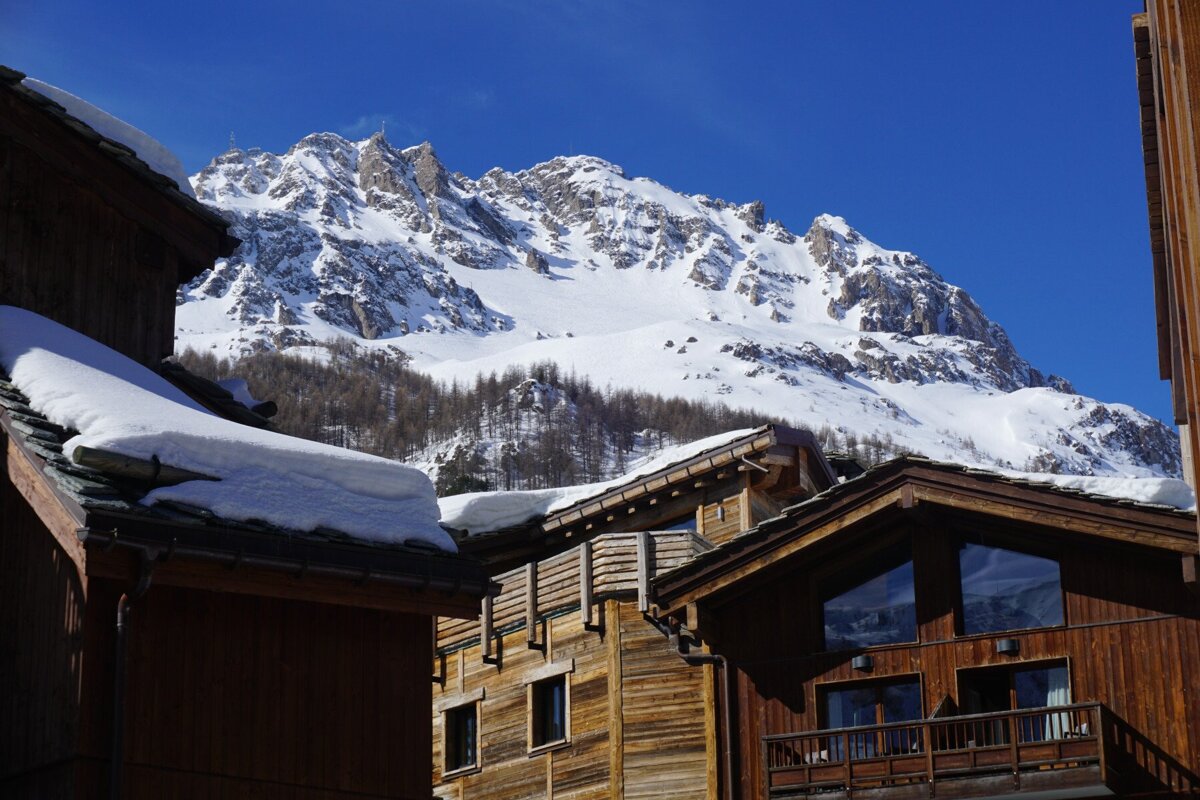 A snowy mountain is behind a row of wooden buildings