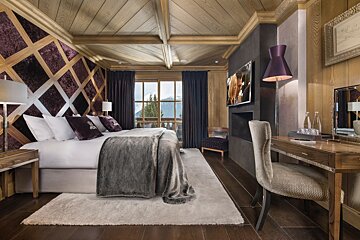 Plush, wood-paneled bedroom with a large bed, mountain views, and a modern TV area, offering a luxurious alpine feel.