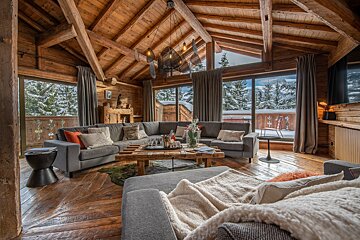 Cozy, rustic wooden living room with large windows showcasing a beautiful snowy mountain landscape and exposed beams.