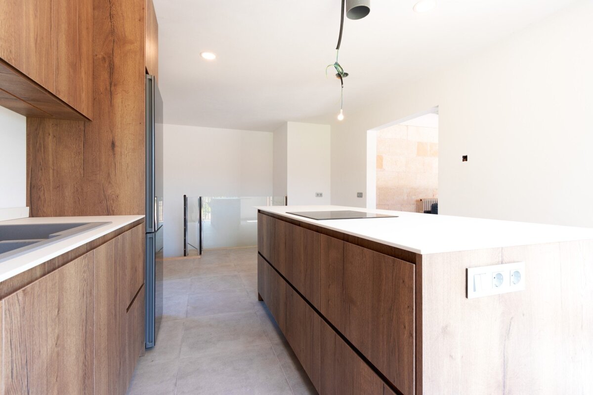 A modern kitchen featuring rich wood grain cabinets, white countertops, and a central island with an induction hob in an open, bright space.