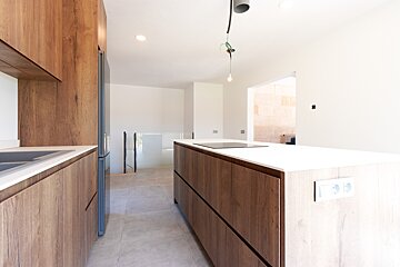 A modern kitchen featuring rich wood grain cabinets, white countertops, and a central island with an induction hob in an open, bright space.