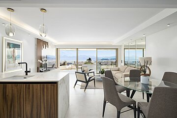 Bright, modern open-plan apartment featuring a kitchen island, dining area, and living room with balcony views of the sea.