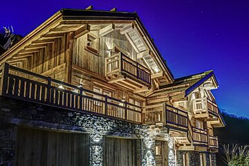 A large wooden house with a balcony is lit up at night