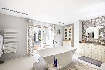 A bright, luxurious bathroom with a freestanding tub, double vanity with mosaic tiles, and glass doors leading to an outdoor patio.