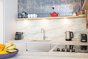 Modern kitchen featuring marble-patterned countertops, a wooden shelf with a red polka dot teapot, and a blue accent wall.