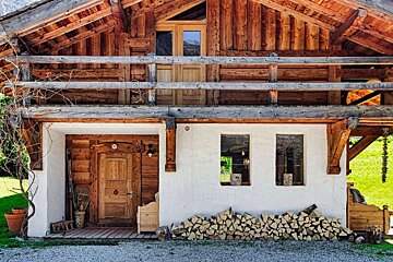 A wooden house with a white wall and a stack of logs in front of it