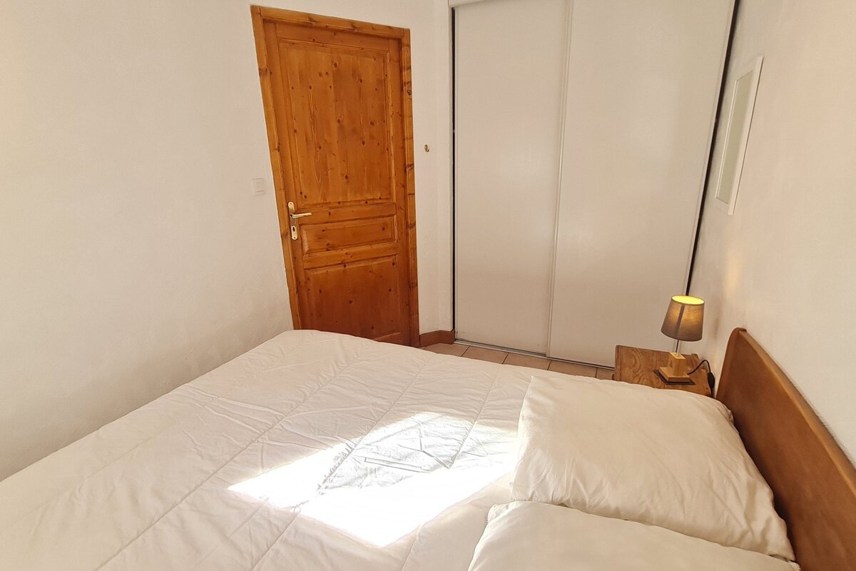 A cozy bedroom featuring a white-covered bed, a wooden door, a white sliding wardrobe, and a lit bedside lamp on a wooden nightstand.