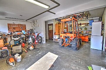 A busy garage filled with an orange tractor with snow chains, a dirt bike, a workbench with tools, chainsaws, and two refrigerators.