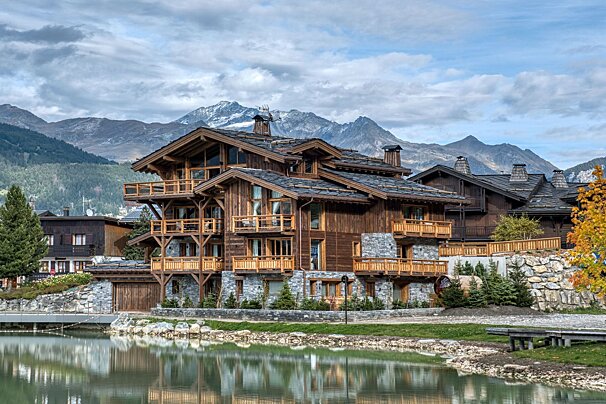 A large house with mountains in the background and a lake in front of it