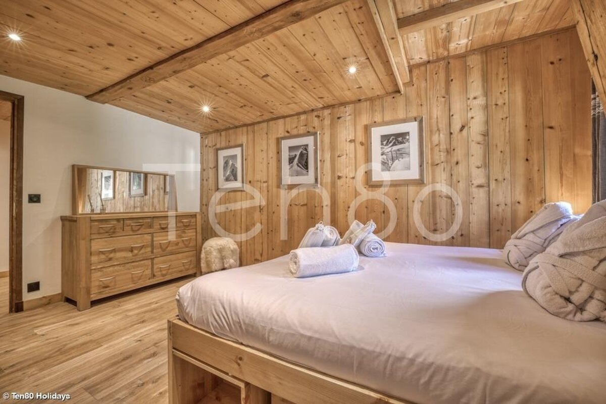 Cozy, rustic cabin bedroom with wood-paneled walls and ceiling, a bed with clean white linens, and a matching wooden dresser.