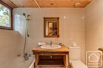 Rustic bathroom with a wooden ceiling, a sink on a wooden vanity, a bathtub, and a mirror reflecting timber rafters.