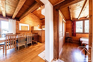 Warm, rustic wooden chalet interior featuring a dining area, kitchen, and a bedroom with a window overlooking mountains.