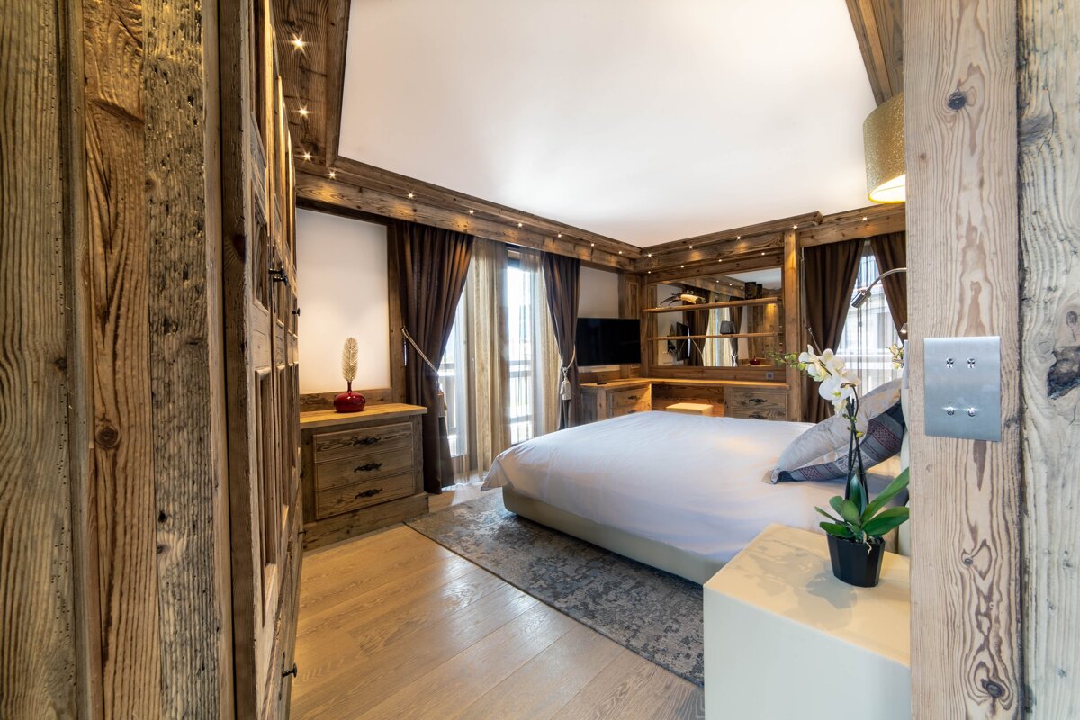 A cozy, modern bedroom featuring extensive rustic wood paneling, a large bed, and warm lighting, giving an alpine chalet feel.