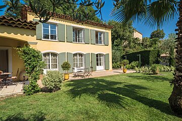 A yellow house with green shutters sits on a lush green lawn