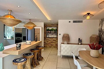 A chic, open-plan organic modern interior features a wood bar with unique tree-stump stools, rattan lamps, sculptural pendant lights, and earthy decor.