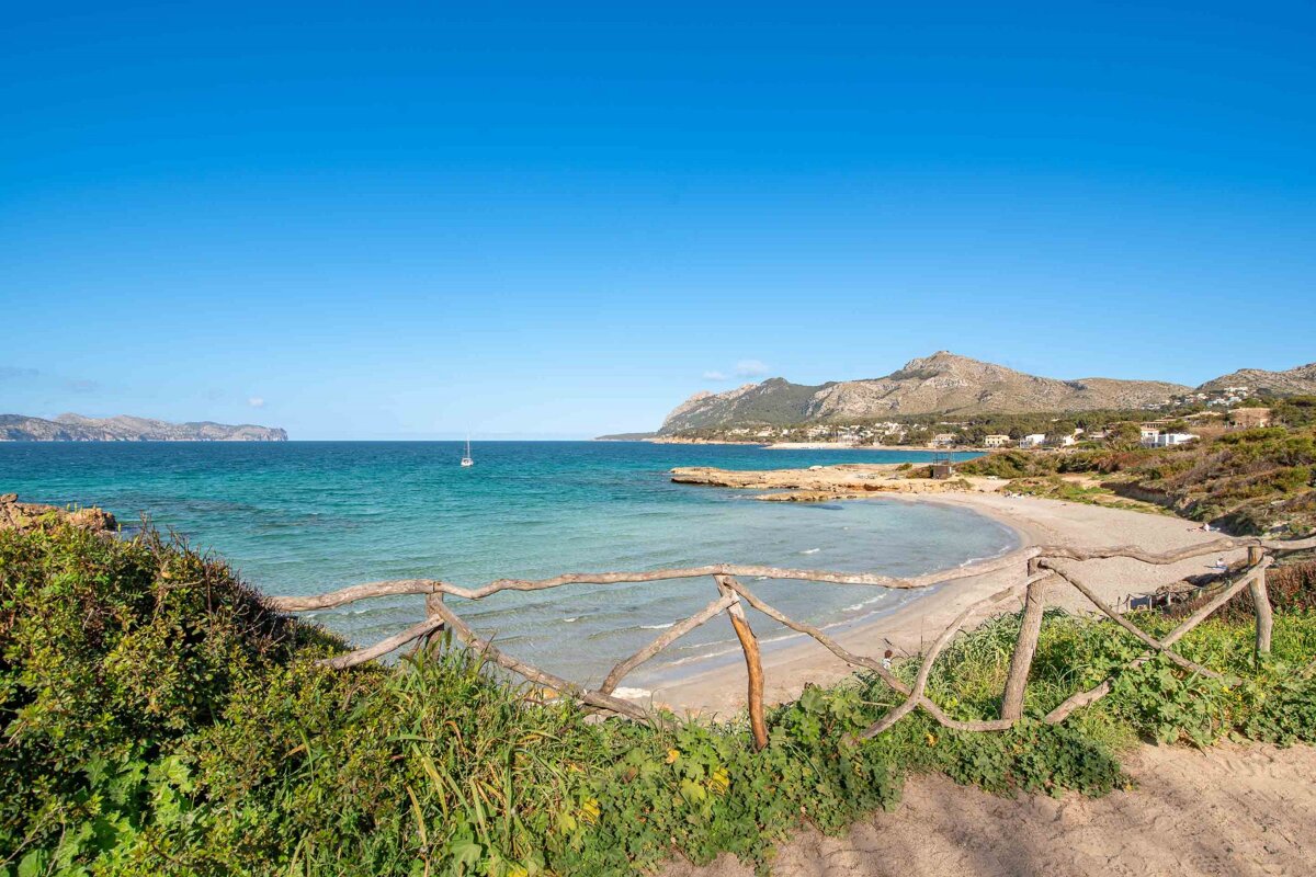 A wooden fence leading to a beach with mountains in the background
