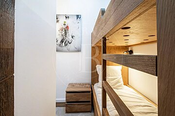 A cozy room features modern wooden bunk beds with built-in lighting, a matching nightstand, white walls, and a dynamic snow sports print.